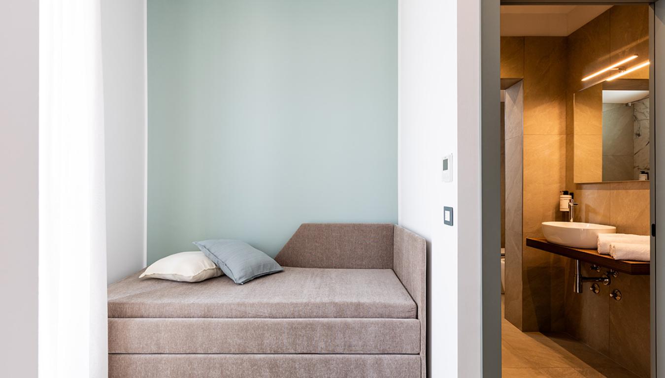 Camera minimalista con letto beige e bagno moderno, atmosfera serena e accogliente.